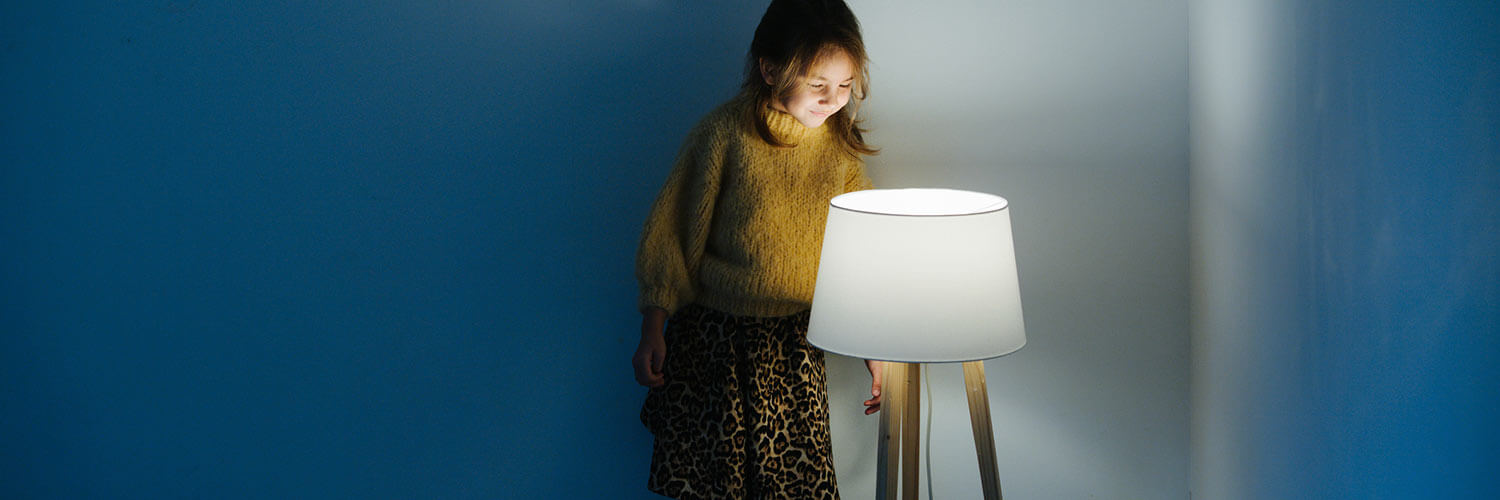 girl standing on the arm of a couch looking at an electric lamp